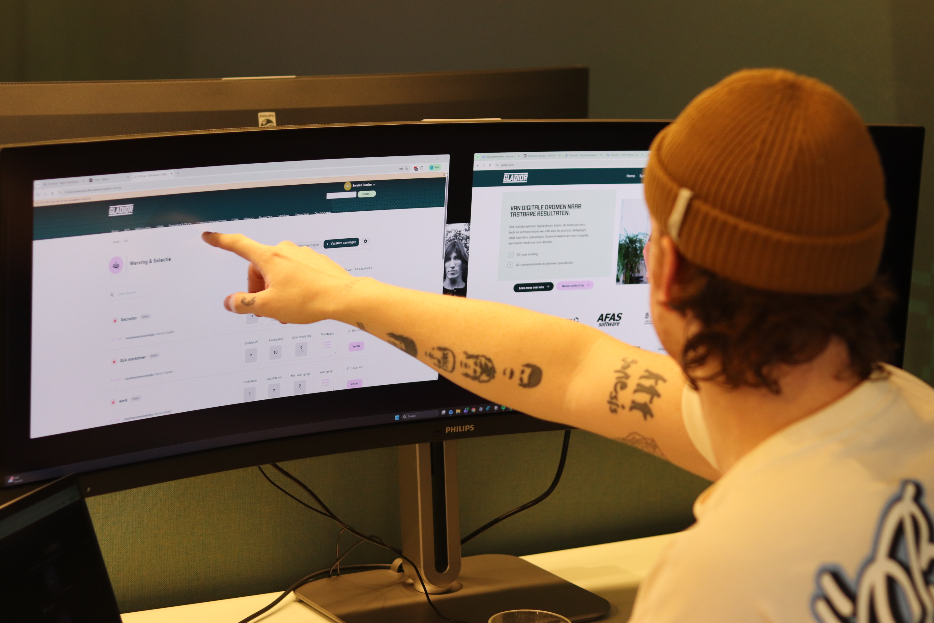 Medewerker wijst naar een recruitmentdashboard op een beeldscherm met daarnaast de website van Gladior op een tweede monitor.