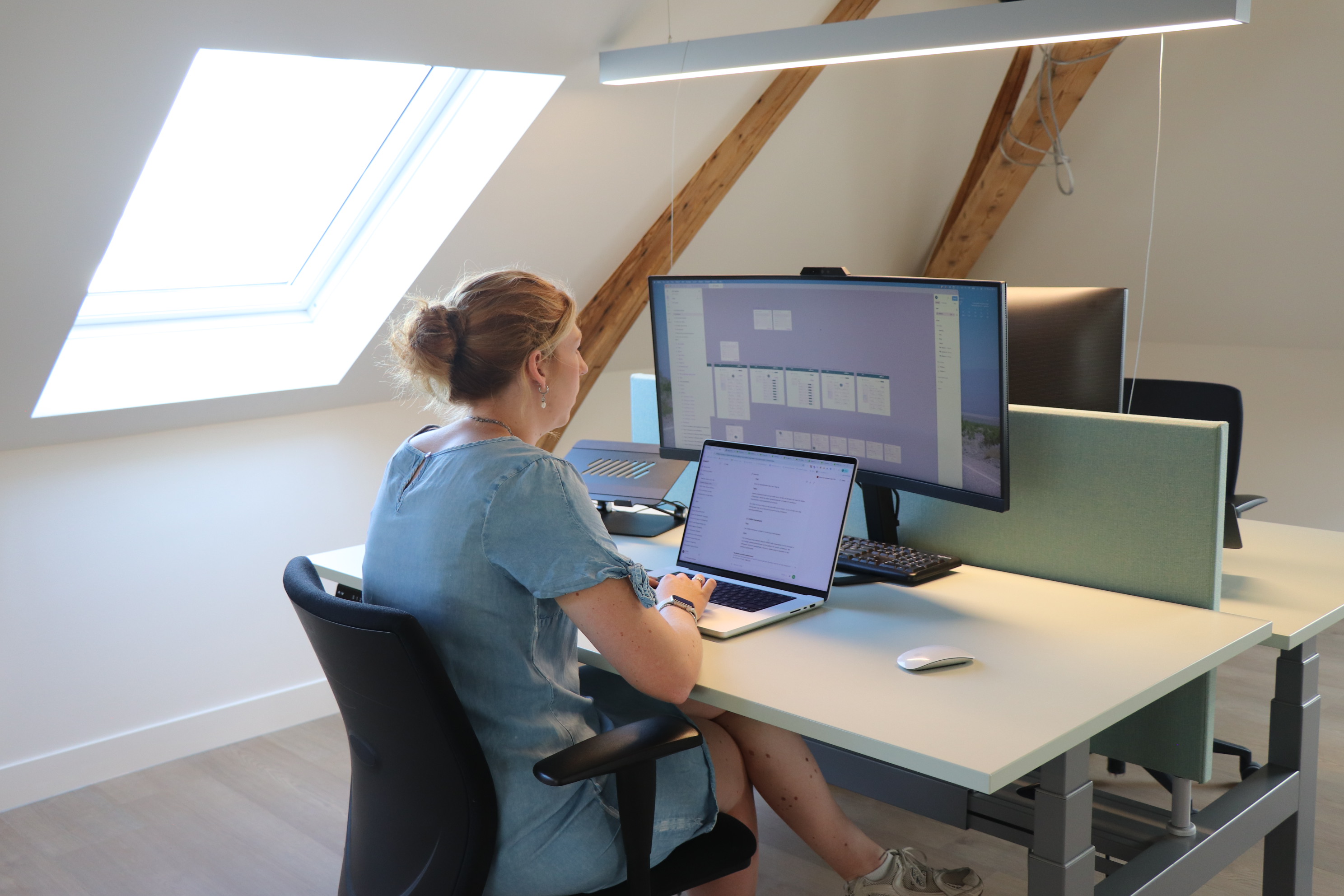 Medewerker werkt achter een laptop en groot beeldscherm aan een digitaal ontwerp op kantoor.