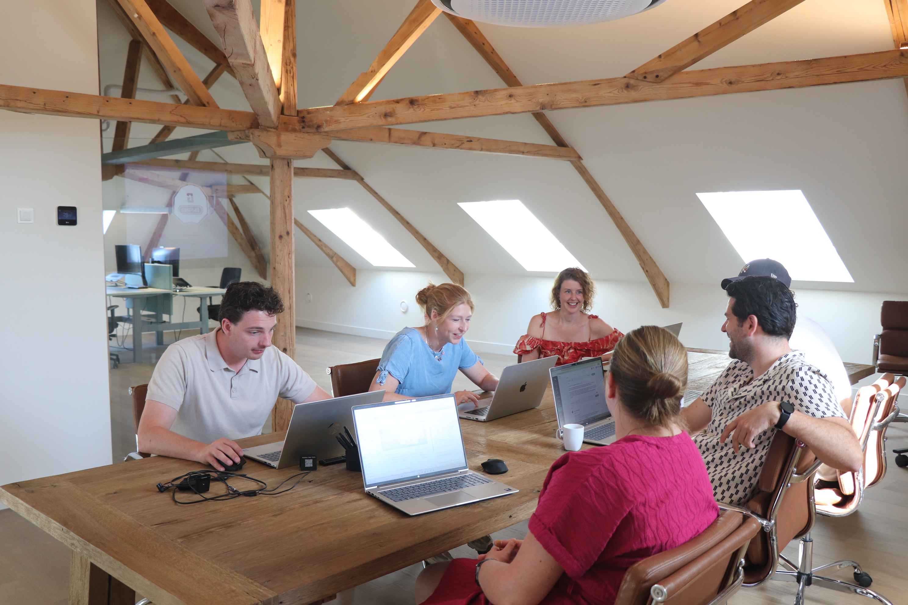 Team zit met laptops aan een grote vergadertafel tijdens een gezamenlijke werksessie op kantoor.