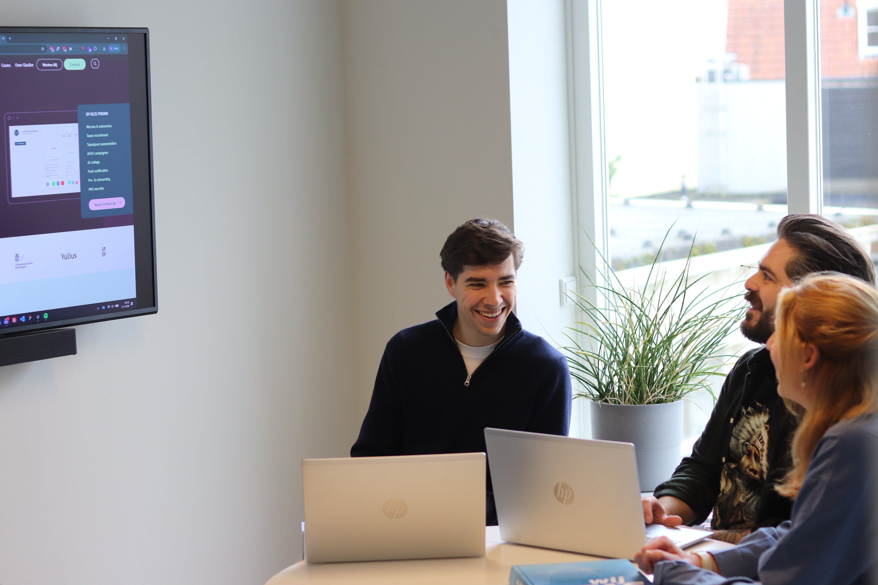 Drie collega’s bespreken lachend een websitepresentatie tijdens een werksessie op kantoor.